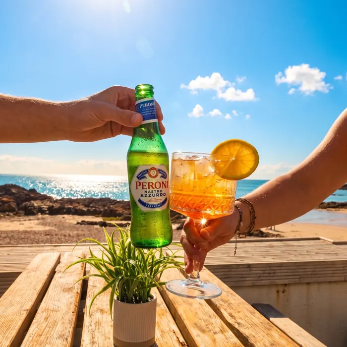 A beer and a cocktail clinked over the beach